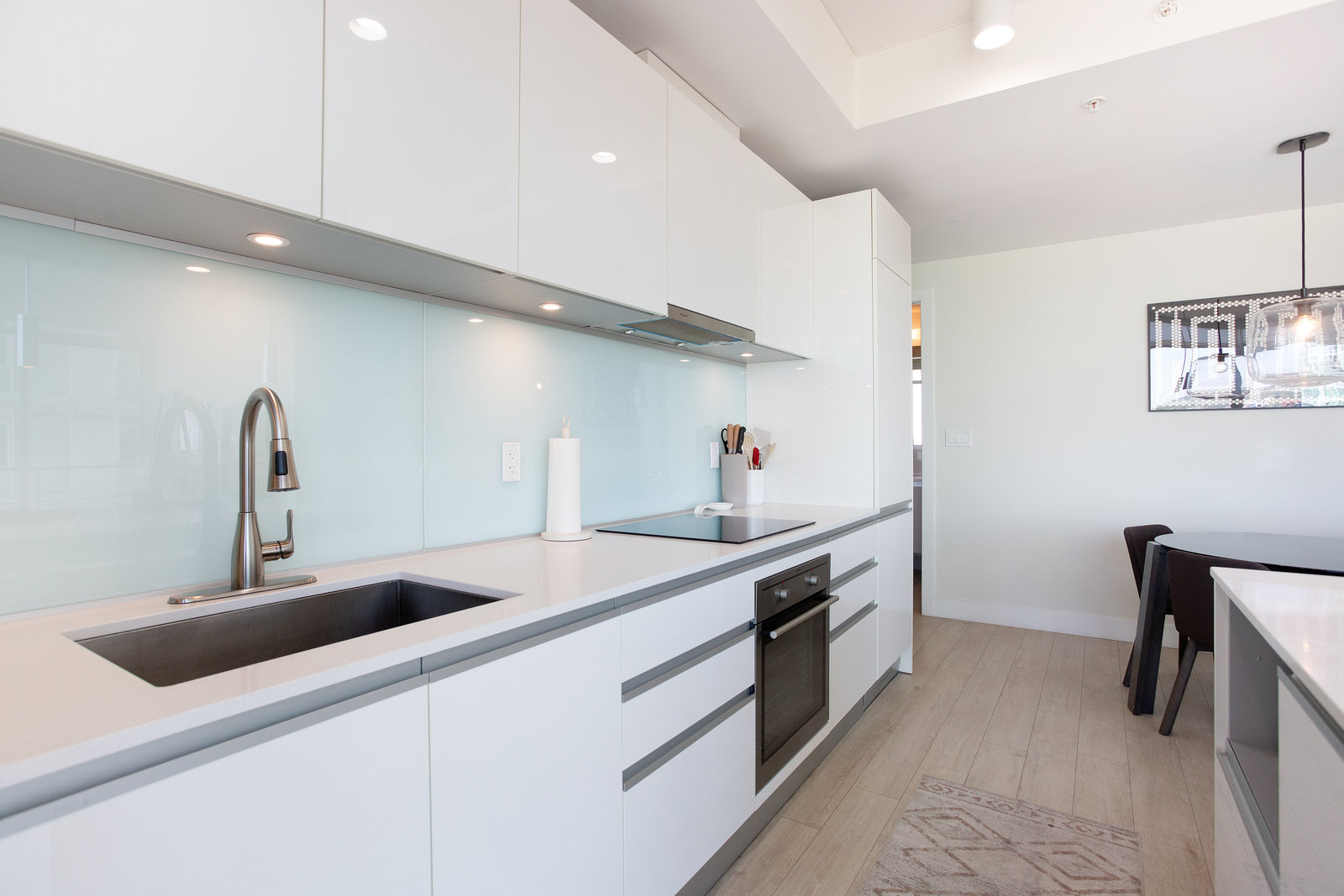 Kitchen sink and white cabinetry with glass backsplash